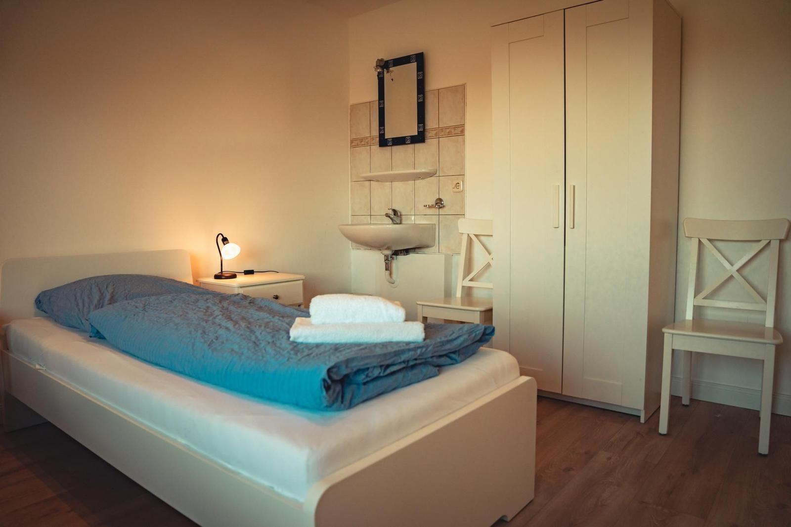 Schlafzimmer mit Bett, Schrank, Waschbecken und Stühlen.