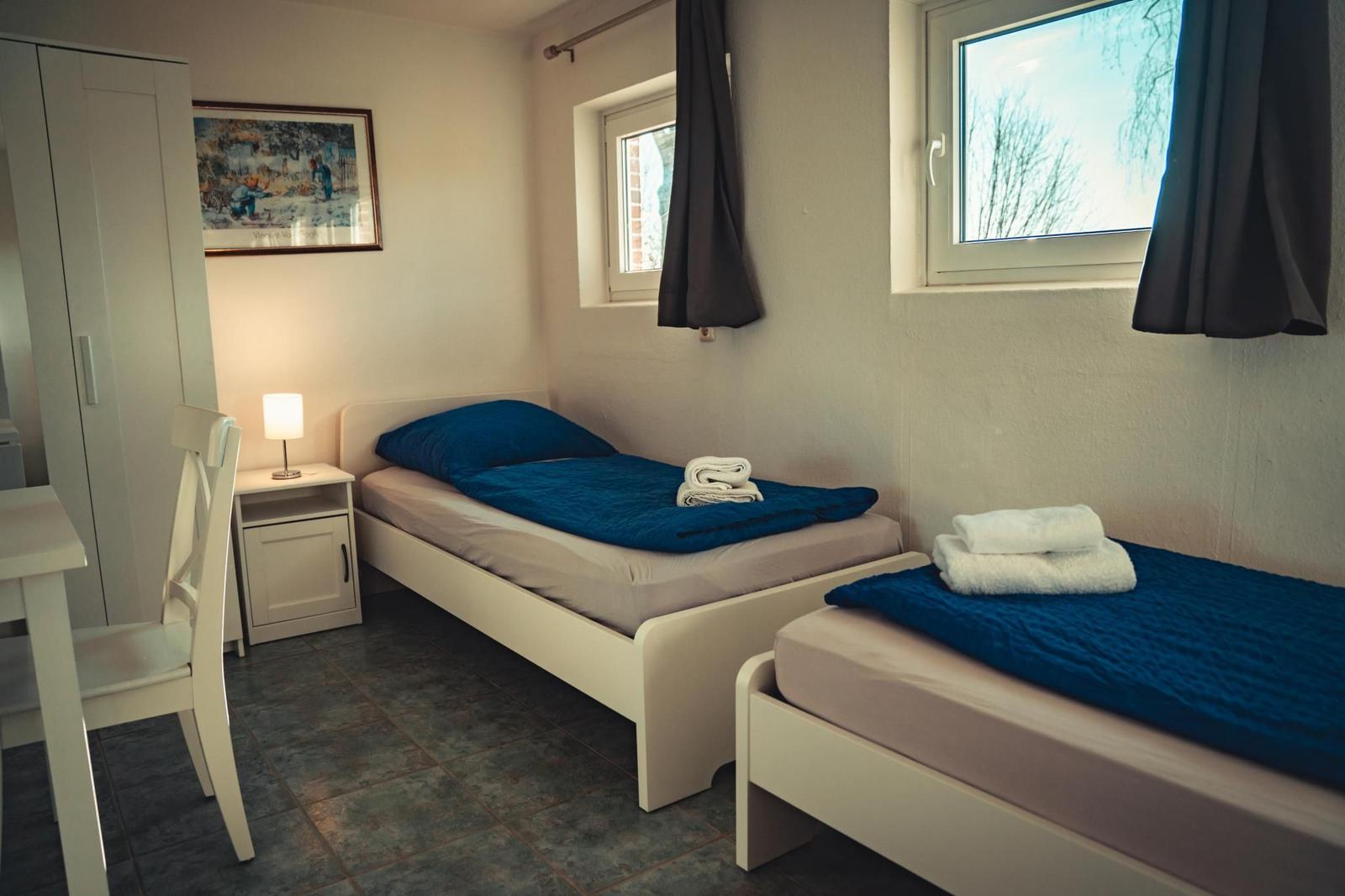 Zwei Einzelbetten mit blauen Bettdecken, Fenster und Schrank im Zimmer.
