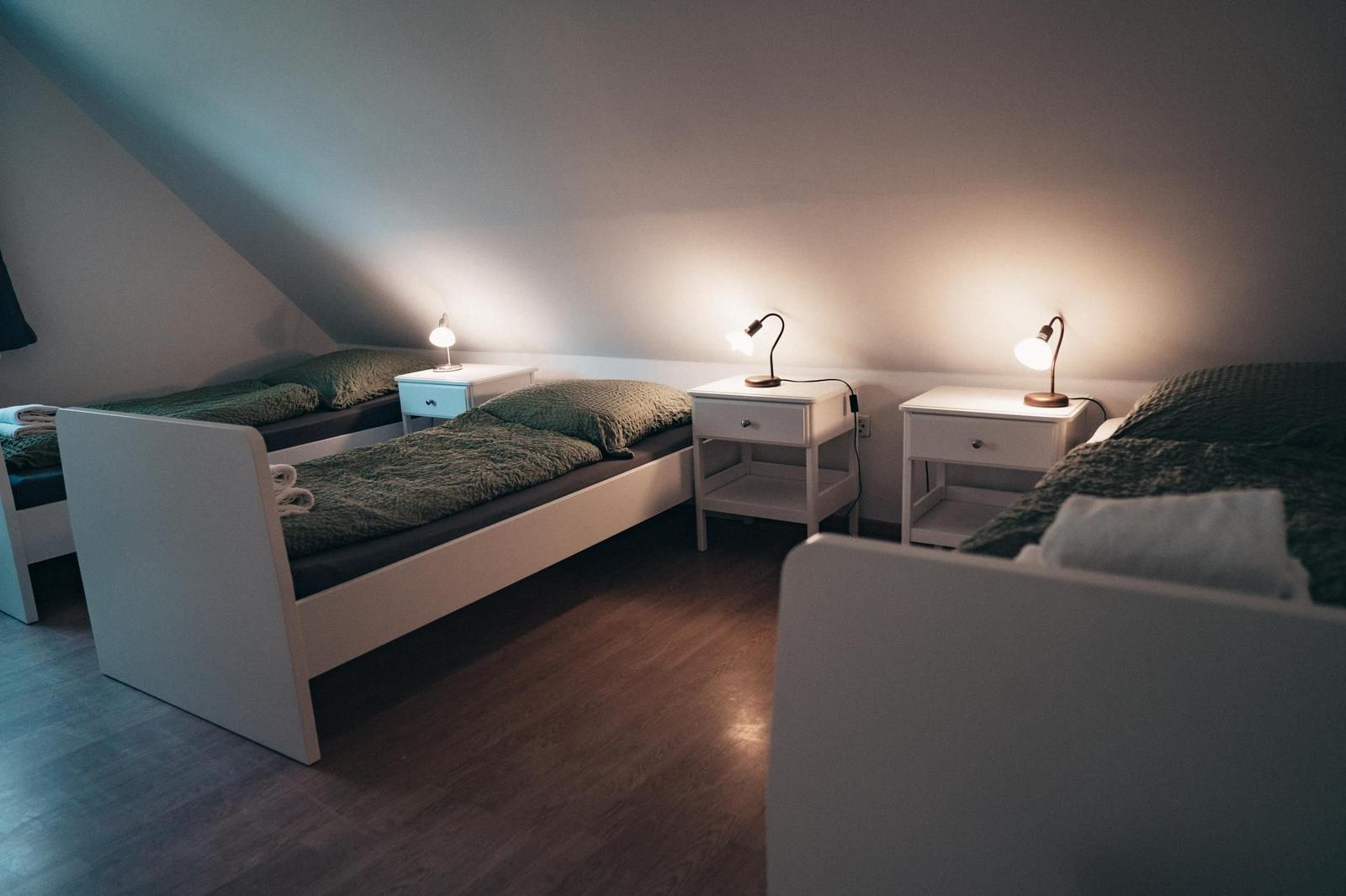 Drei Betten mit Nachttischen und Lampen unter schrägem Dach