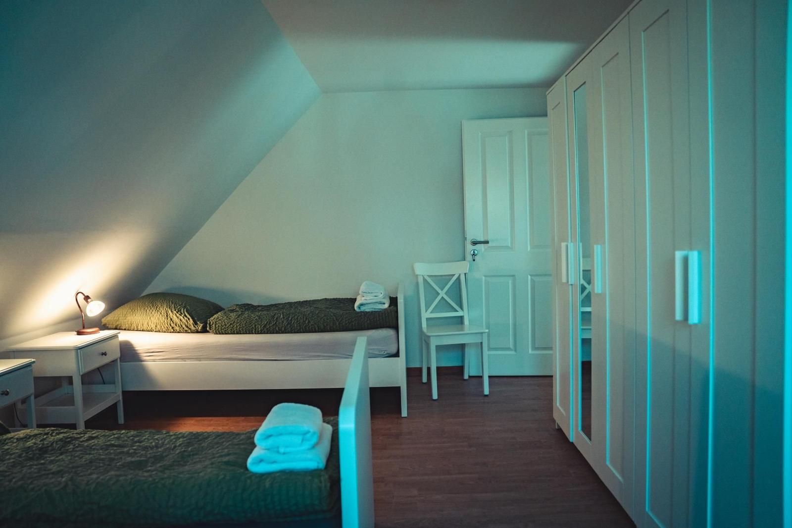 Zimmer mit zwei Betten, Schrank, Stuhl und Nachttisch unter Dachschrägen.