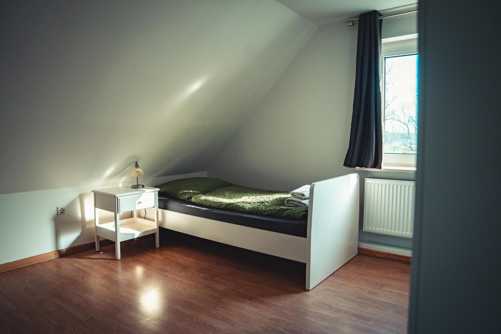 Schlafzimmer mit Dachschrägen, Bett, Nachttisch und Fenster mit Vorhang.