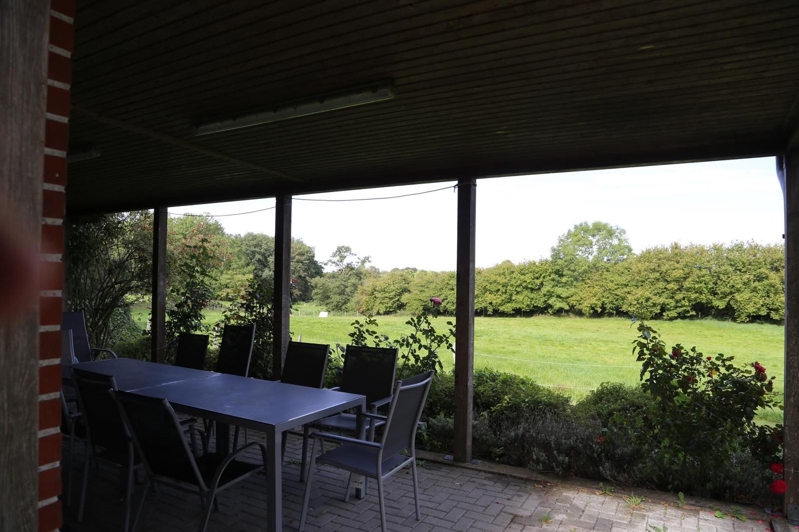 Terrasse mit Tisch und Stühlen, Blick auf grünes Feld und Bäume.