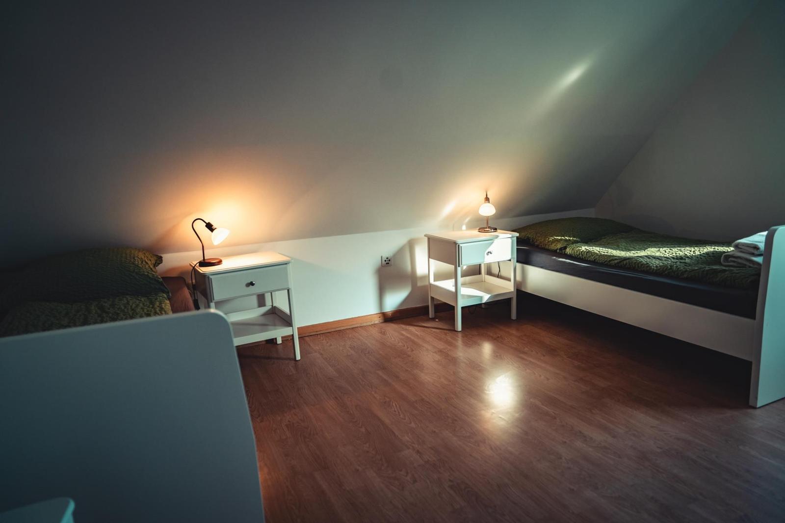 Zimmer mit zwei Betten, Nachttischen und warmem Licht unter Dachschrägen.
