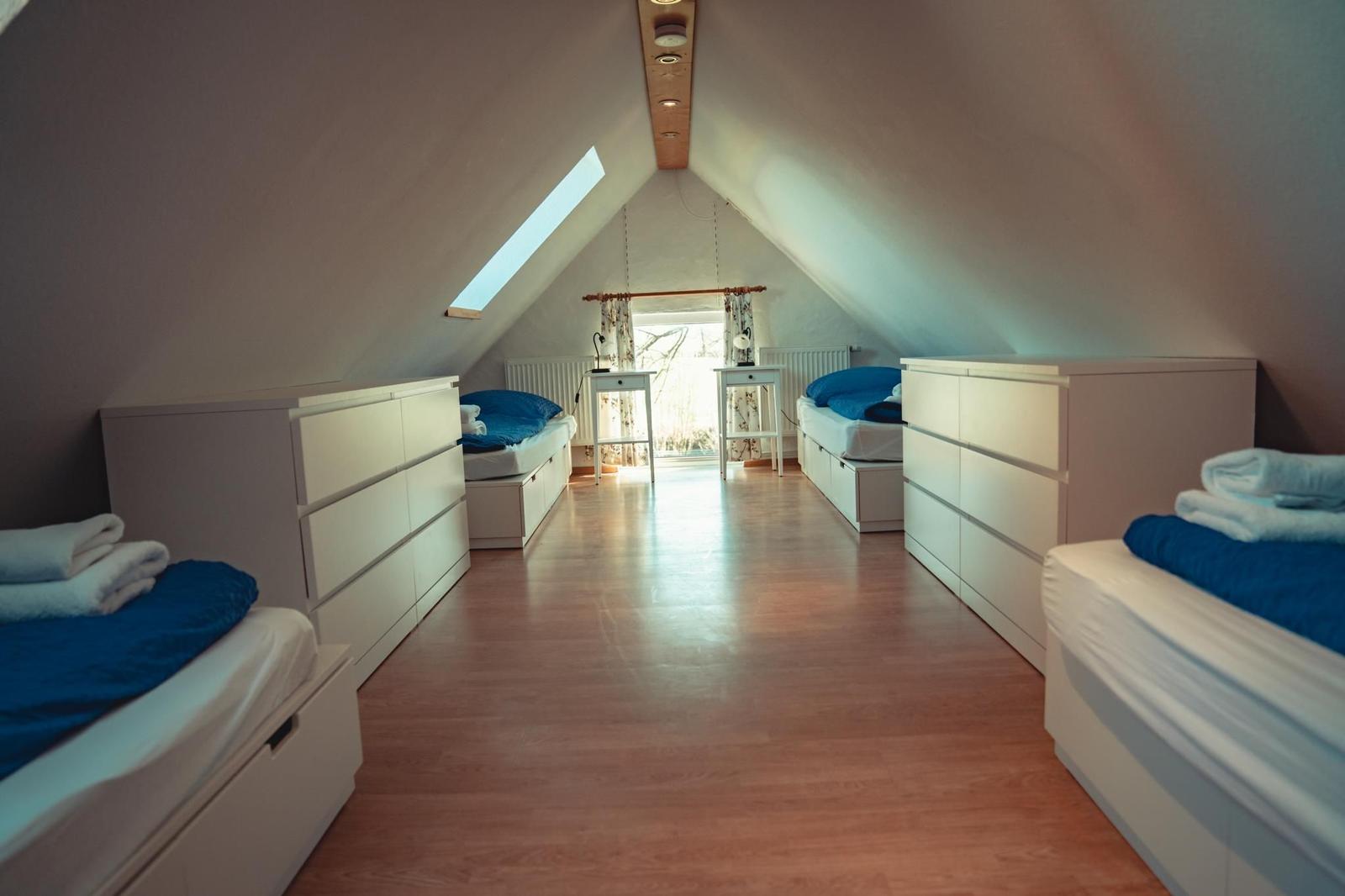 Dachgeschosszimmer mit drei Betten, Schränken und Holzboden. Fenster und Dachfenster.