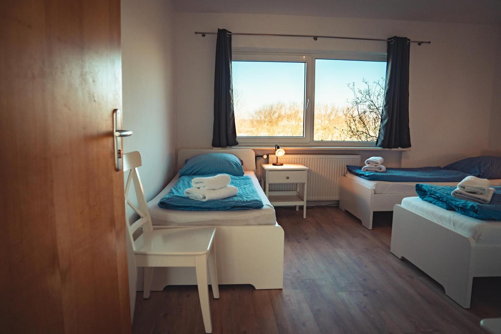 Zimmer mit drei Betten, Fenster und Holzboden.