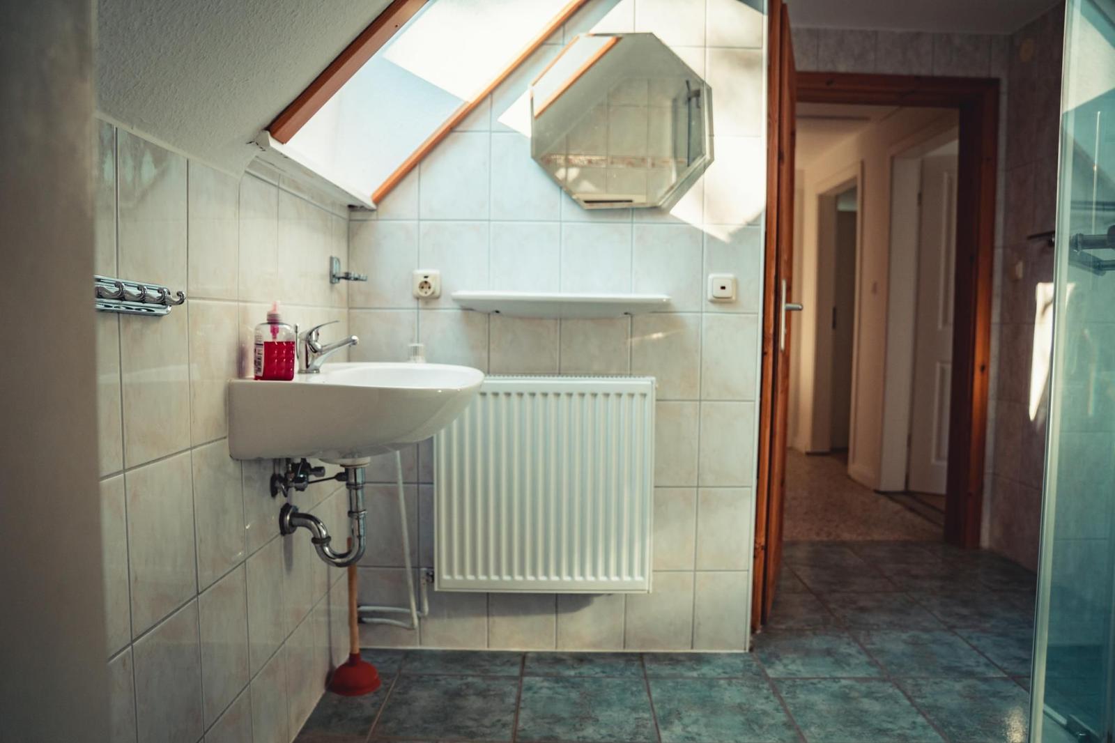Badezimmer mit Waschbecken, Spiegel und Dusche unter Dachschrägen.