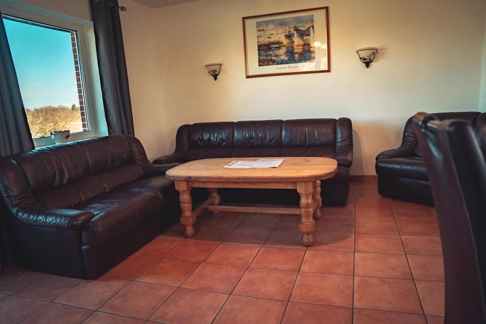 Wohnzimmer mit Ledersofa, Holztisch und Wandbild. Fenster mit Blick auf Außen.