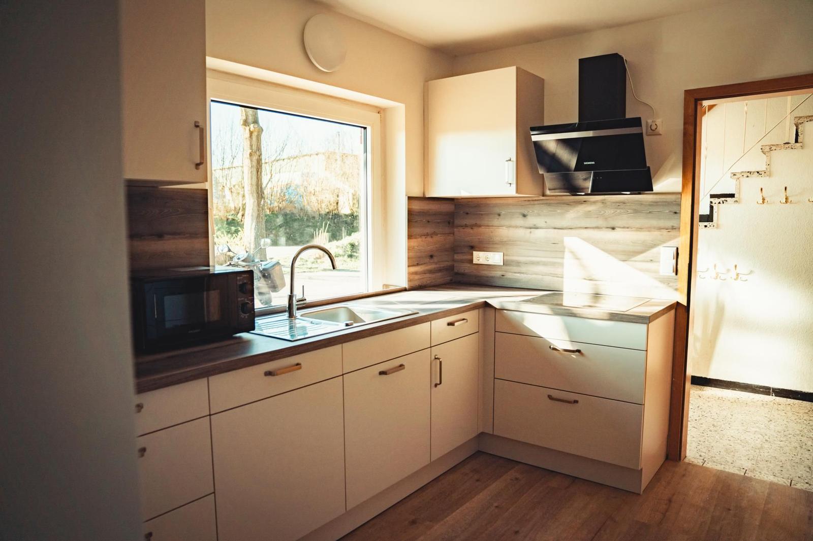 Küche mit Fenster, Spüle, Mikrowelle und Holzrückwand.