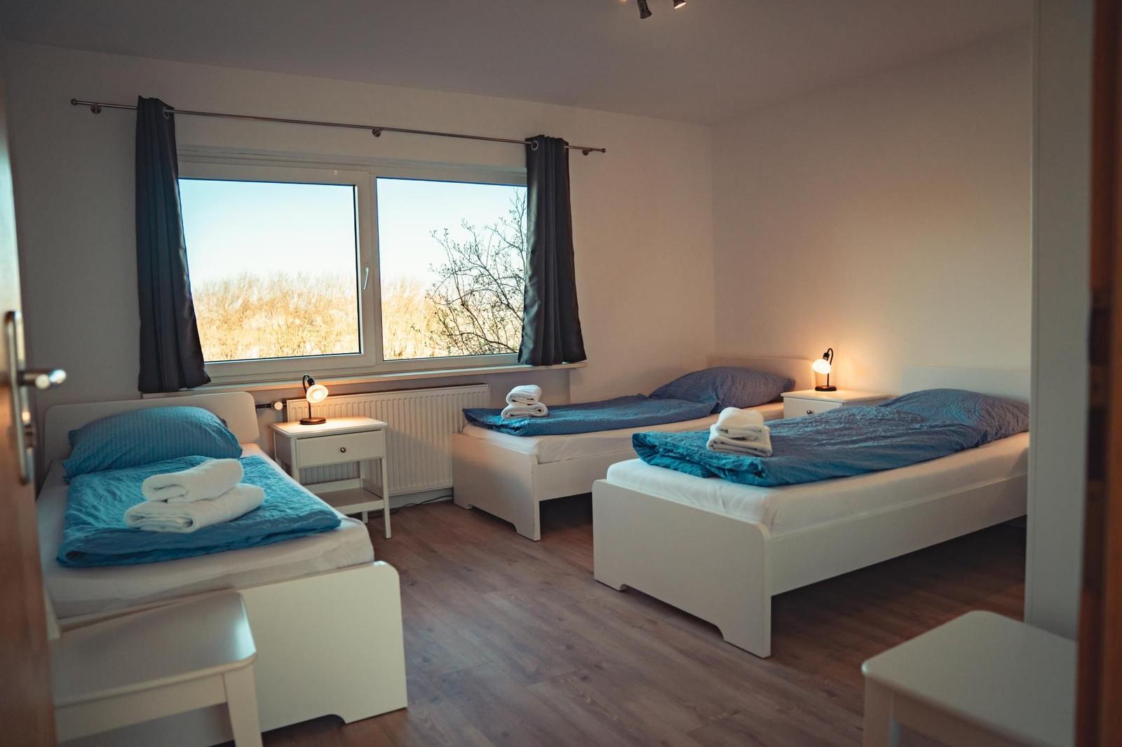 Zwei Einzelbetten mit blauen Bettwäschen und Nachttischen unter einem Fenster.