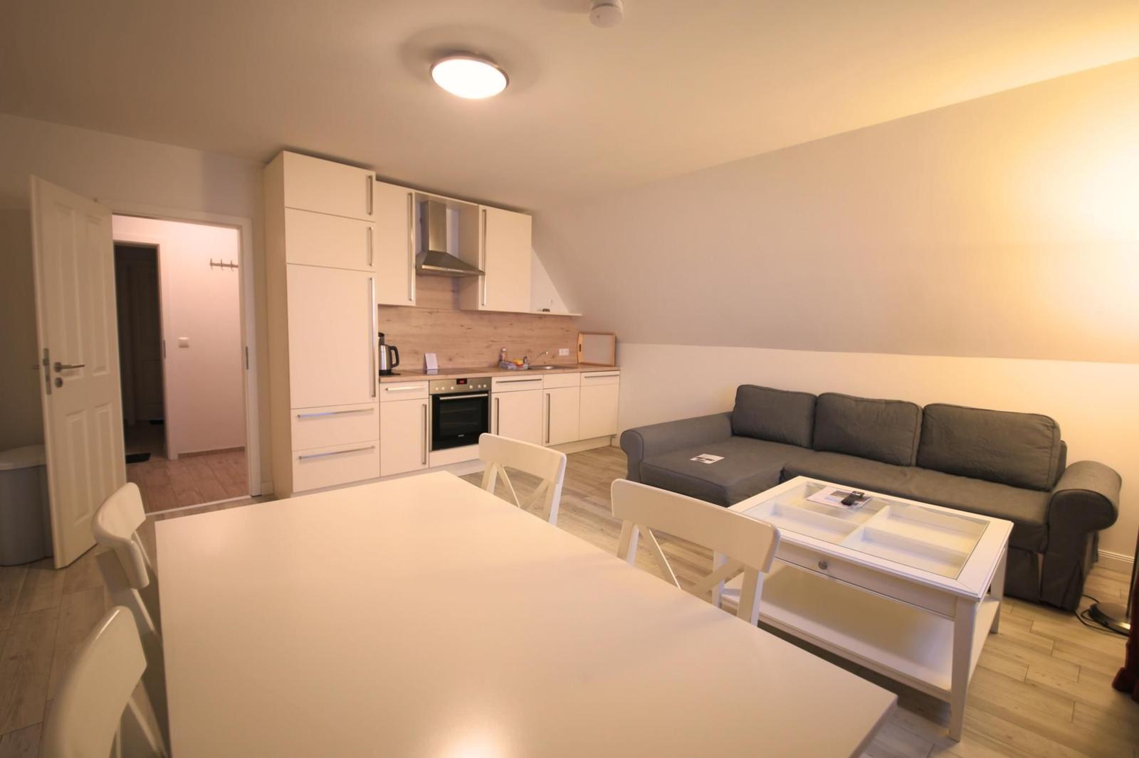 Wohnküche mit grauem Sofa, weißem Tisch und Küchenschränken.