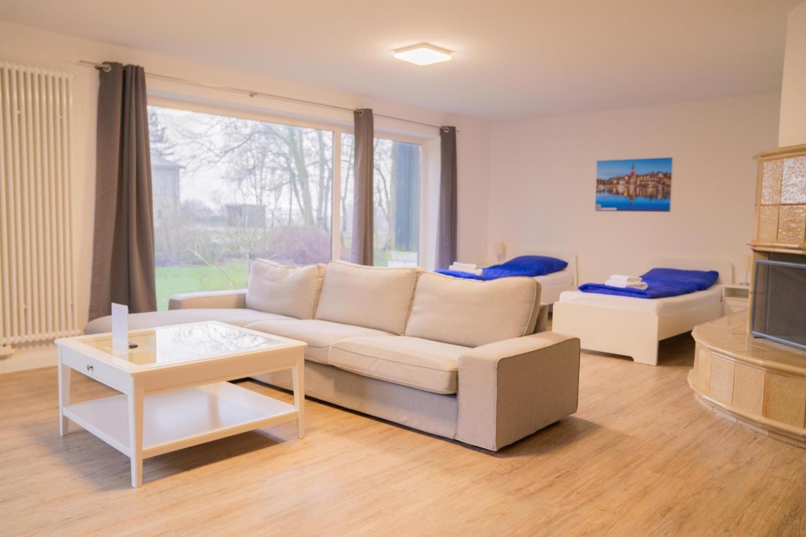 Wohnraum mit Sofa, zwei Betten und großem Fenster. Holzboden und Wandbild.