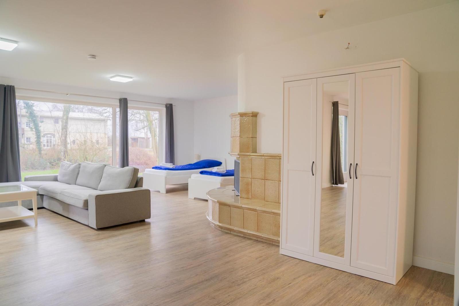 Wohnraum mit Sofa, Bett und Kleiderschrank. Holzboden und Fenster mit Blick.