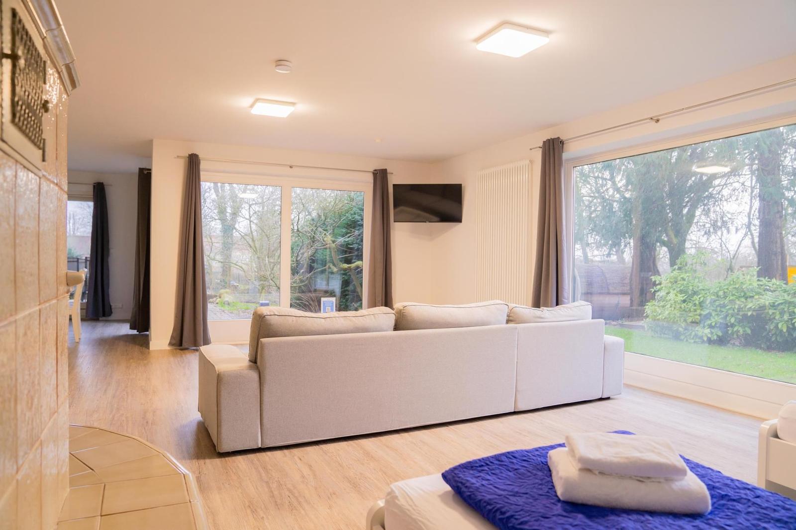 Wohnzimmer mit Sofa, TV und großen Fenstern zum Garten
