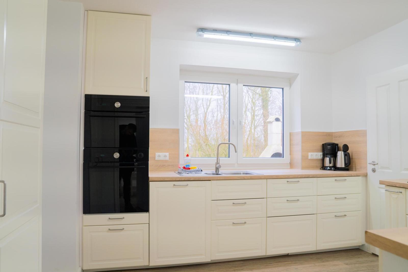 Küche mit weißen Schränken, Edelstahlspüle und Fenster zum Garten.