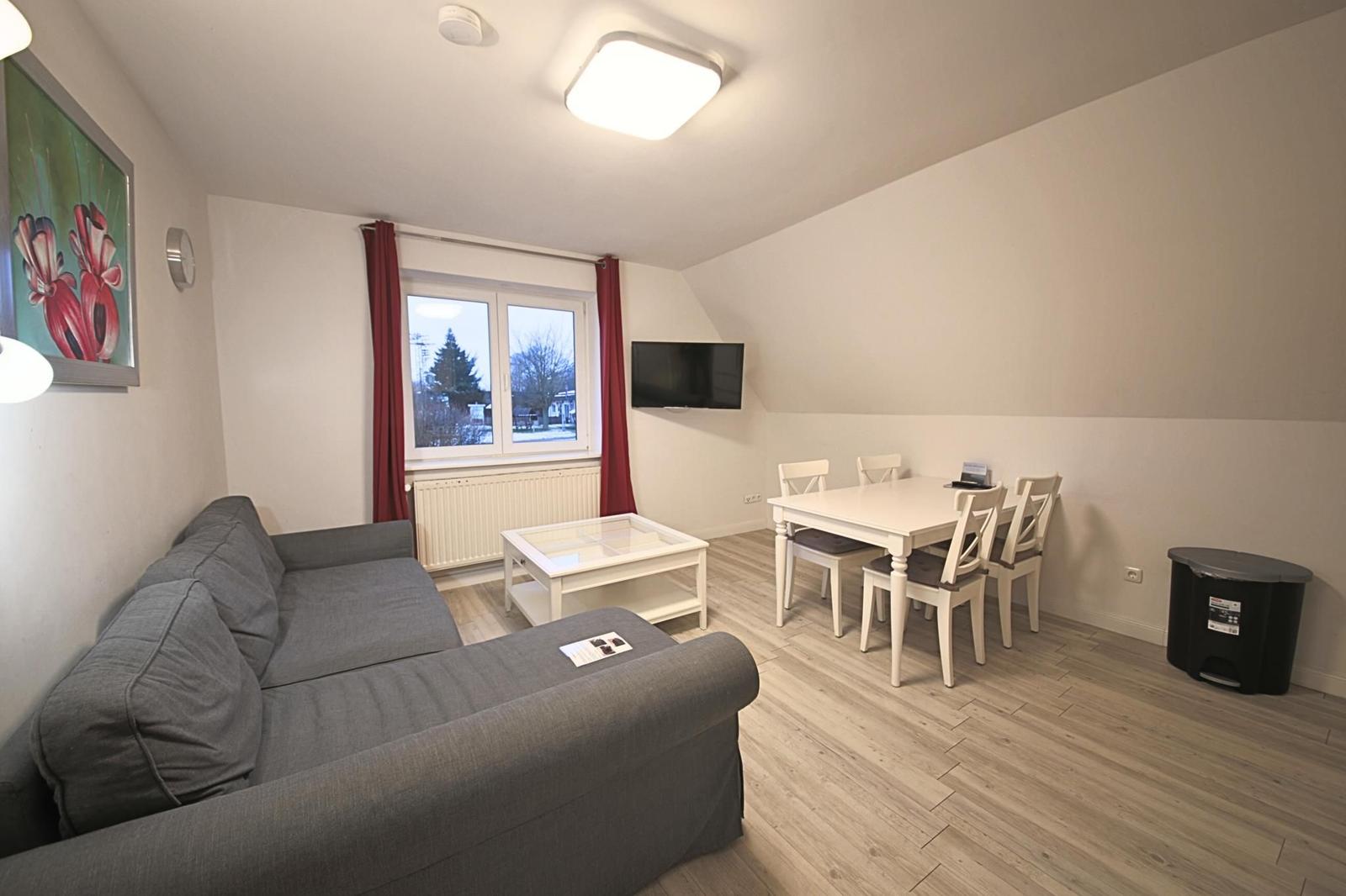 Wohn- und Essbereich mit Sofa, Esstisch und TV. Fenster mit roten Vorhängen.