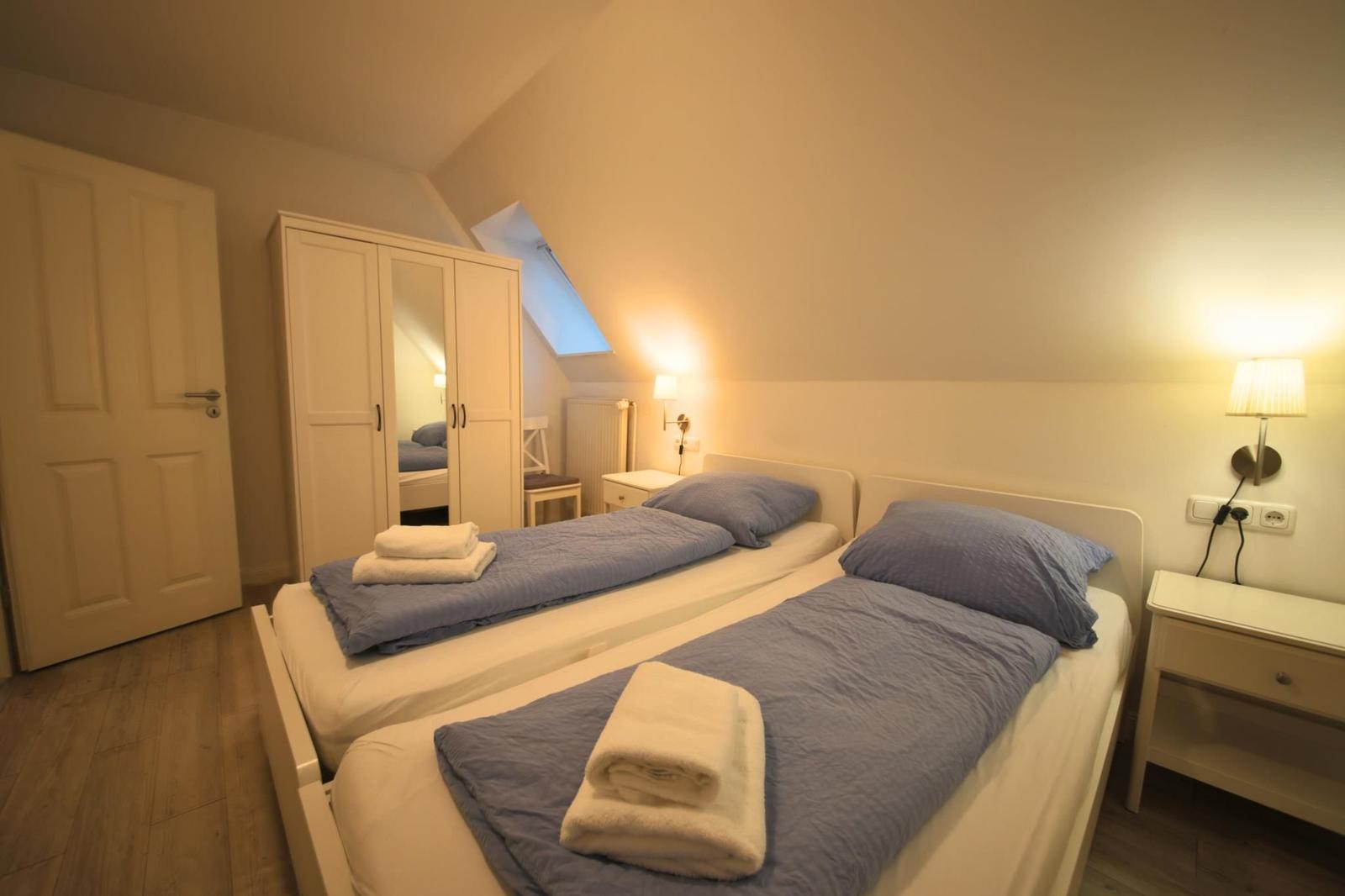 Zwei Betten mit blauen Bettwäschen und Handtüchern. Schrank, Nachttisch und Dachschrägen.