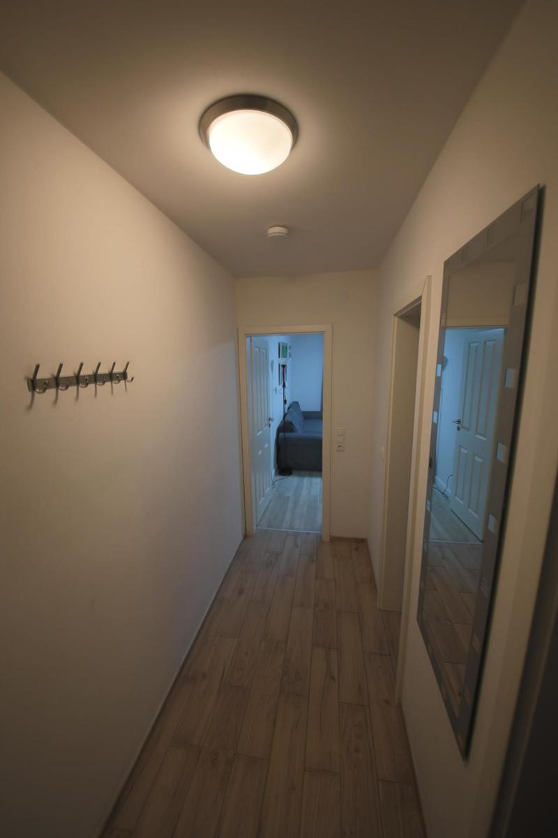 Flur mit Holzboden, Hakenwand und Spiegel. Durchgang zu Wohn- und Schlafzimmer.