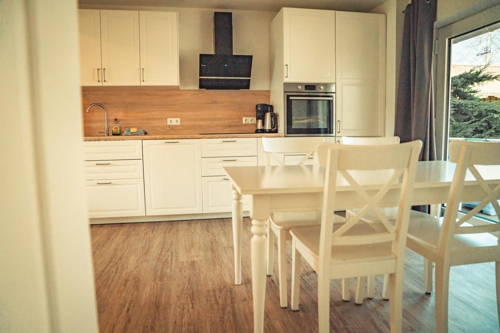 Küche mit Esstisch und weißen Stühlen. Holzfußboden und weiße Schränke.
