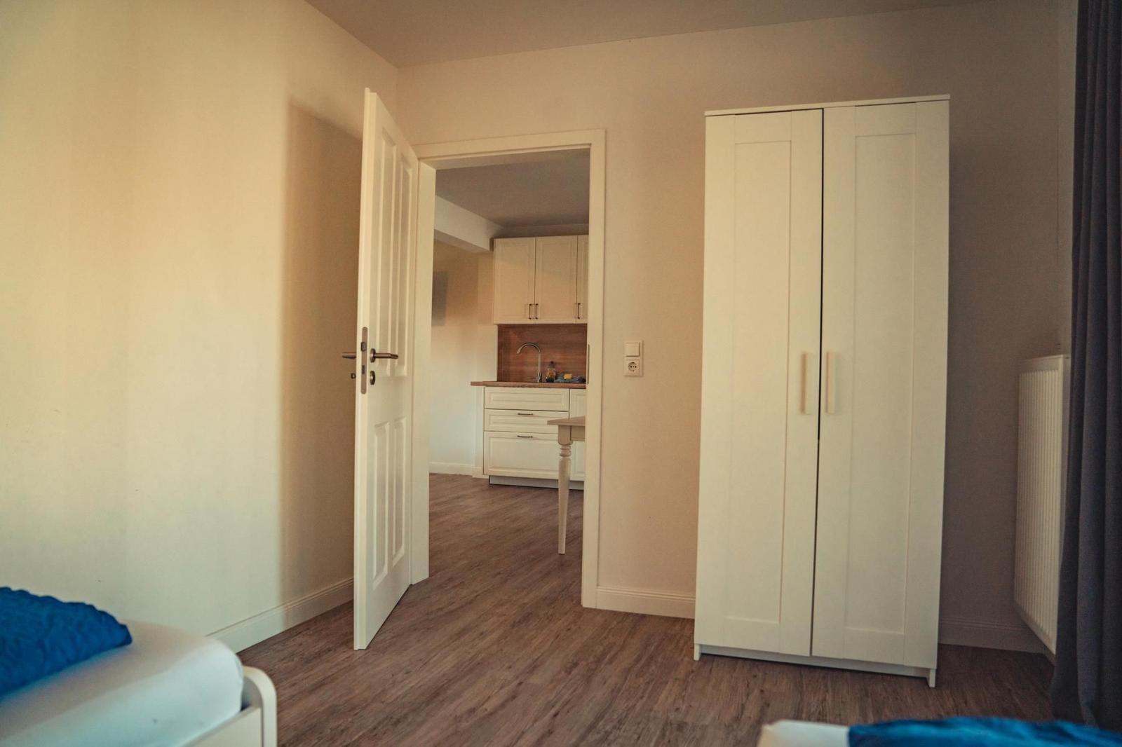 Schlafzimmer mit Kleiderschrank und Tür zum angrenzenden Küchenbereich.