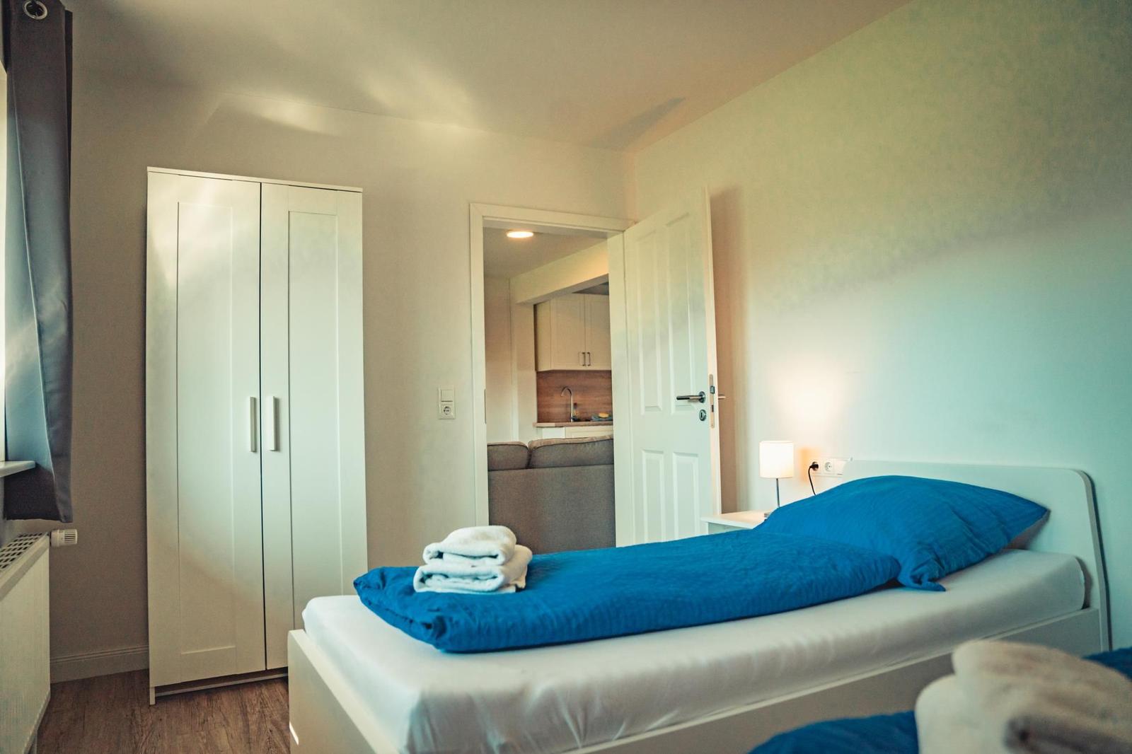 Schlafzimmer mit Bett, Schrank und Blick in die Küche.
