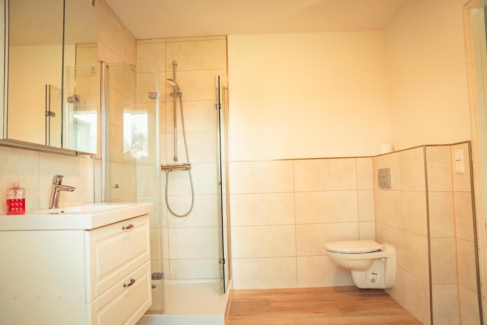 Bad mit Dusche, Waschbecken und WC. Fliesenwand und Holzboden.