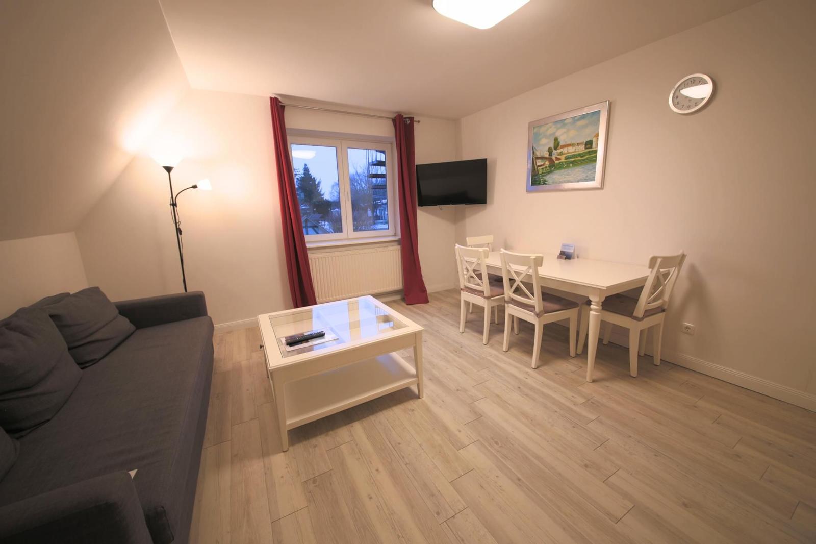 Wohn- und Essbereich mit Sofa, Esstisch, Fernseher und Fenster mit roten Vorhängen.