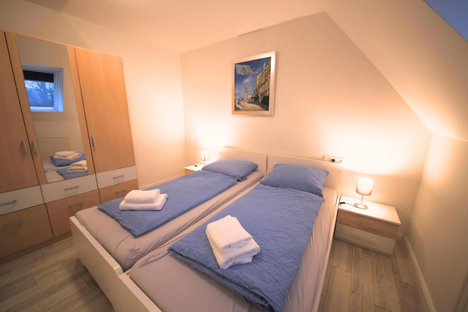 Zimmer mit zwei Betten, Schrank und Nachttisch mit Lampe.