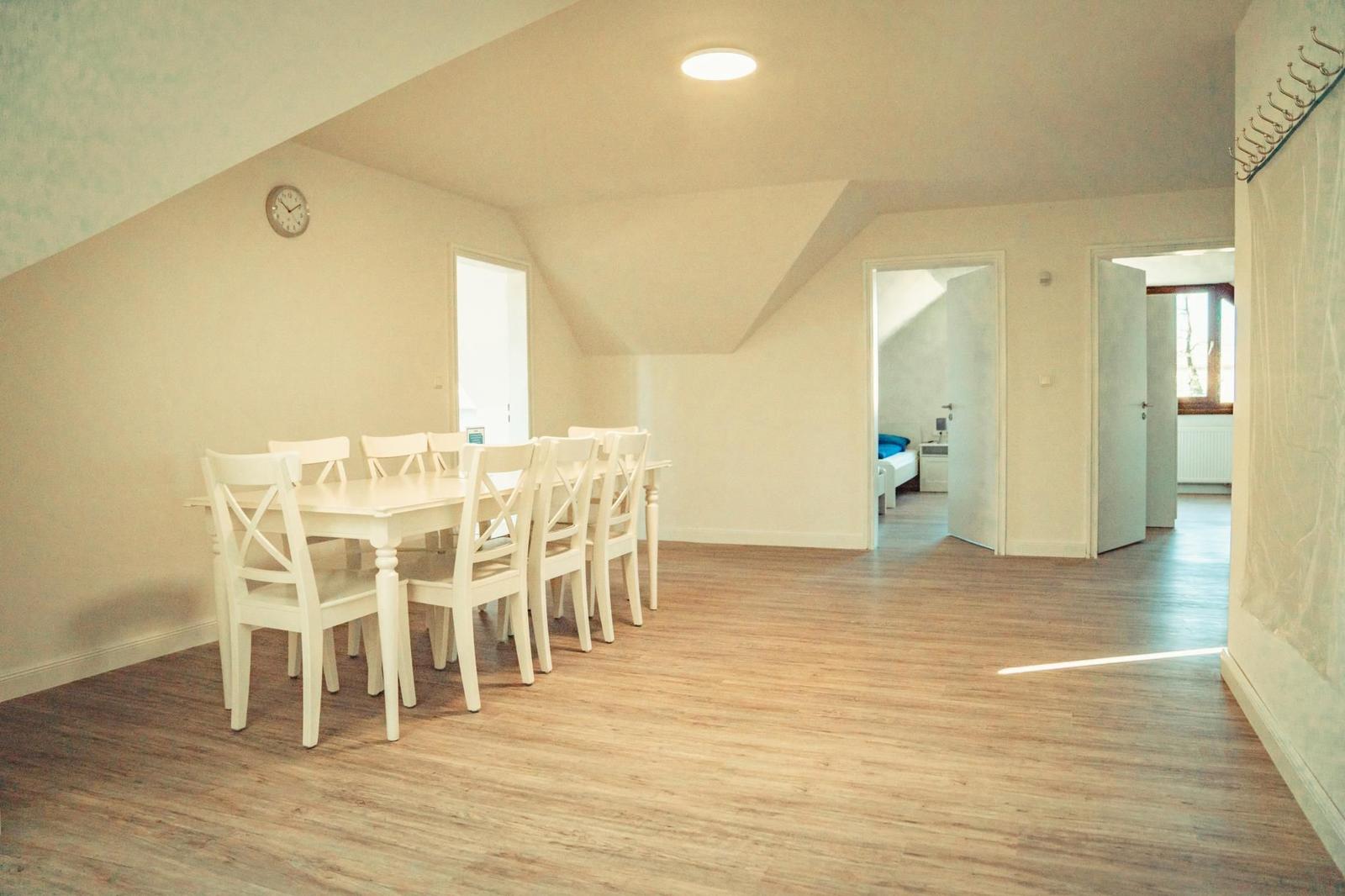 Esszimmer mit weißem Tisch und Stühlen, Holzboden und Sicht auf Schlafzimmer.