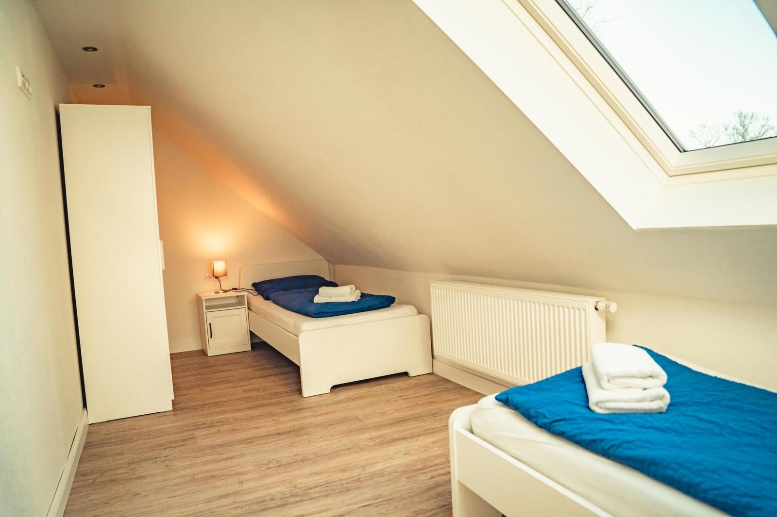 Zimmer mit zwei Betten, Dachschräge und Dachfenster. Holzfußboden und weißer Schrank.