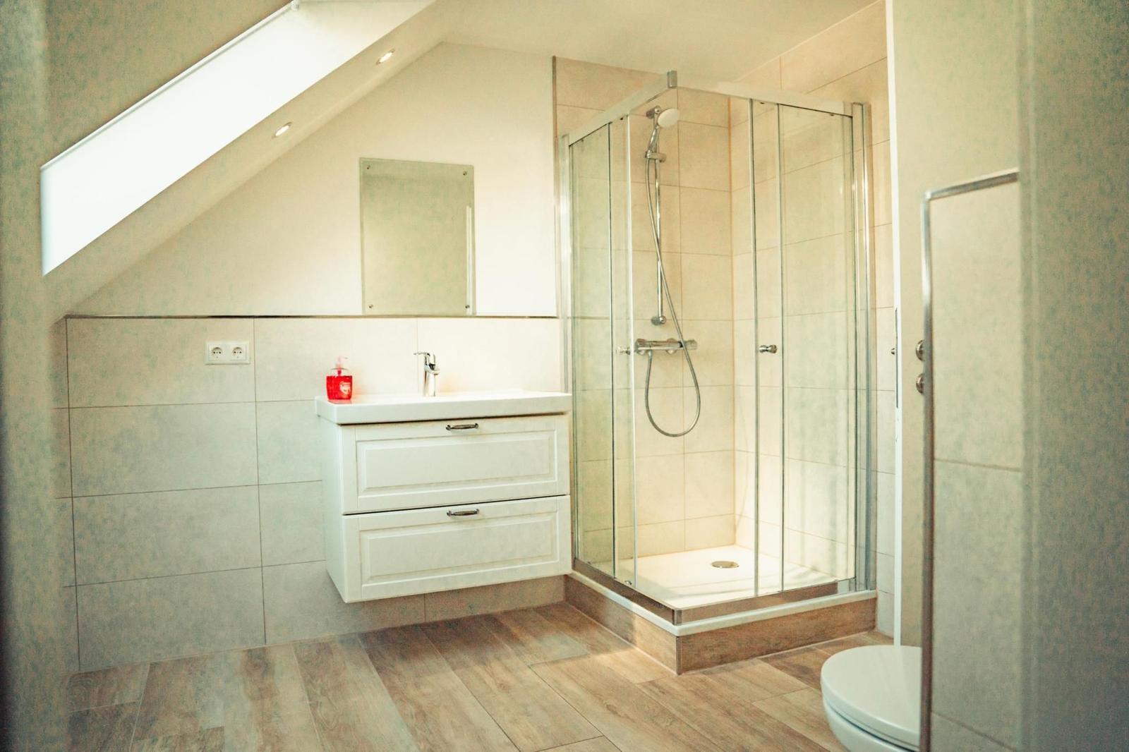 Badezimmer mit Dusche, Waschbecken und Toilette unter Dachschräge.