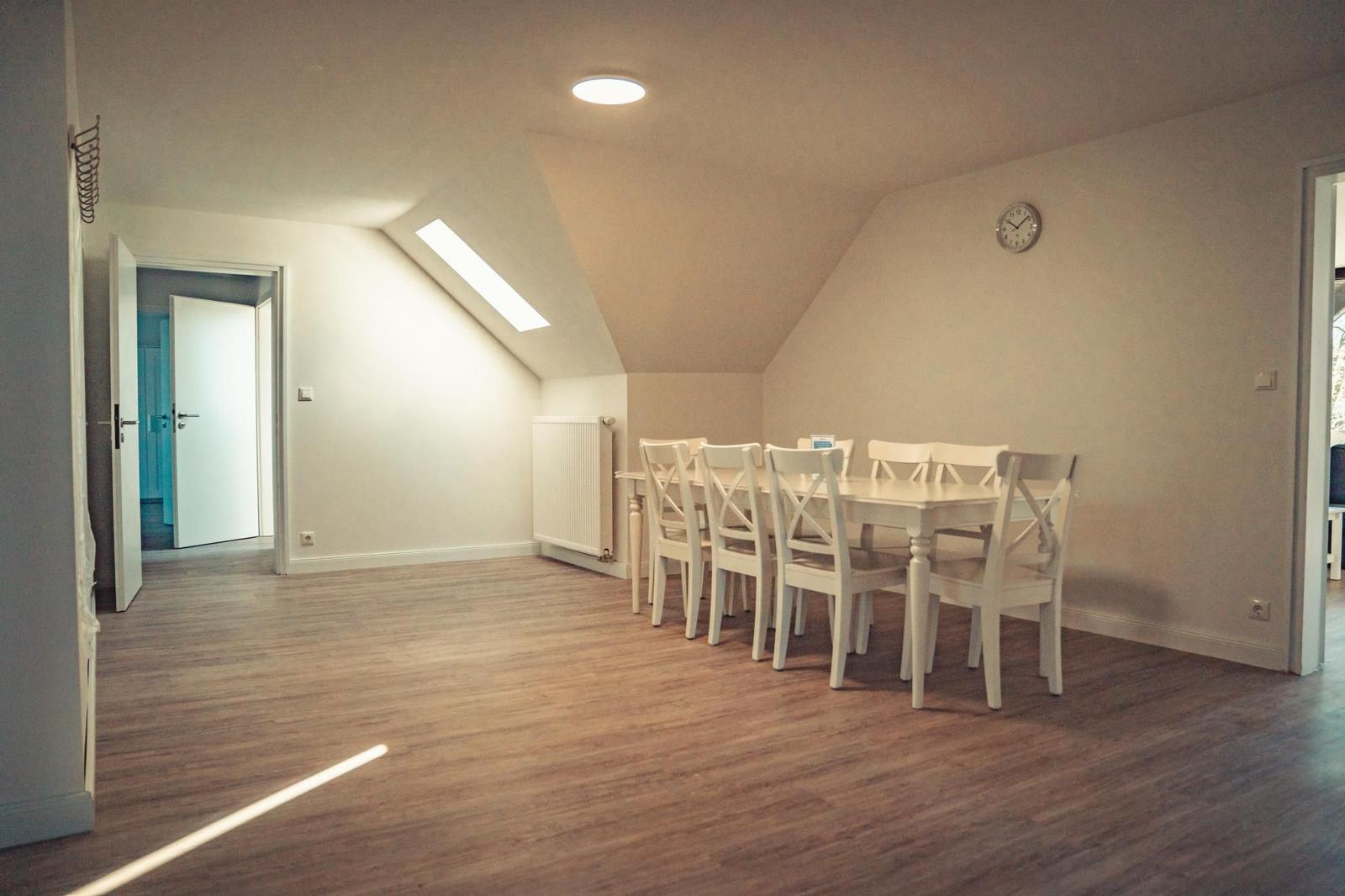 Esszimmer mit weißem Tisch und Stühlen, Holzboden und Dachschrägen.