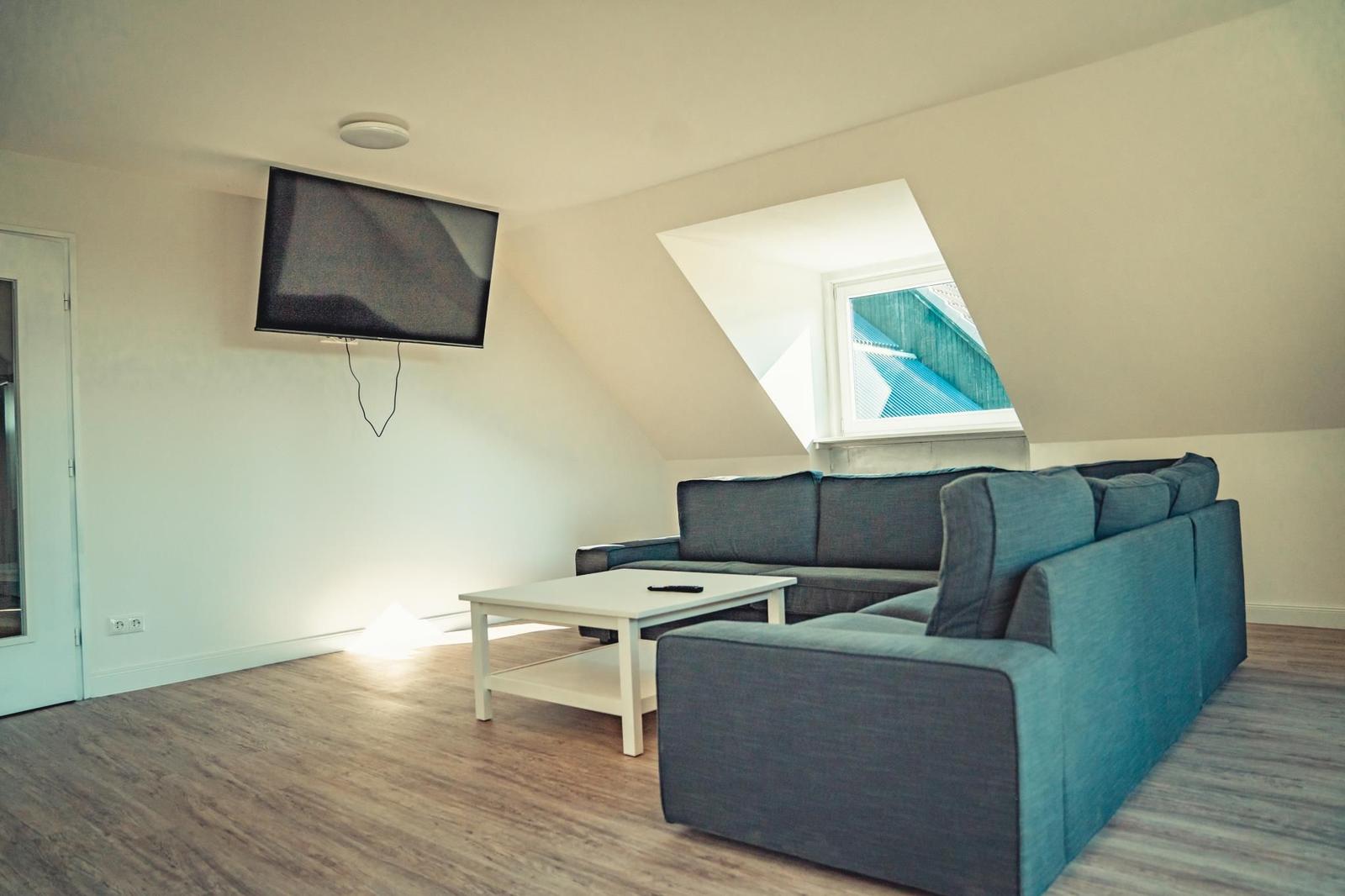 Wohnzimmer mit Sofa, Couchtisch und Wand-TV unter Dachschrägen.