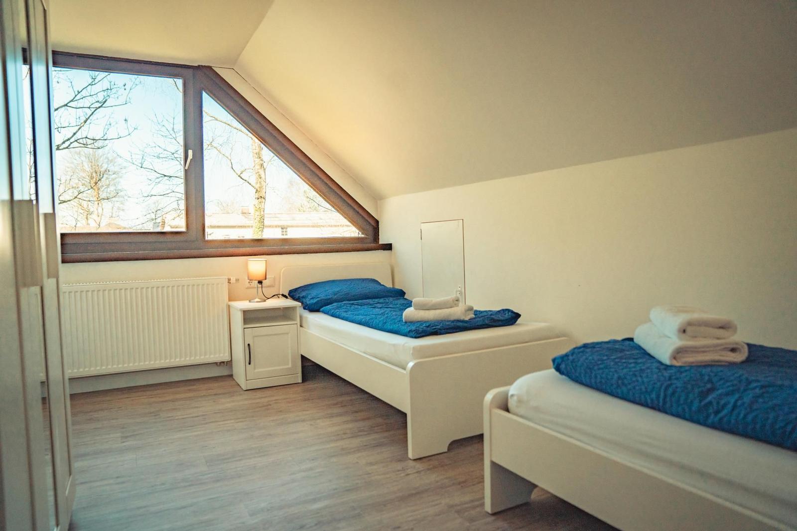 Zwei Einzelbetten mit blauen Bettwäschen und Handtüchern. Dachfenster, Heizkörper und Nachttisch.