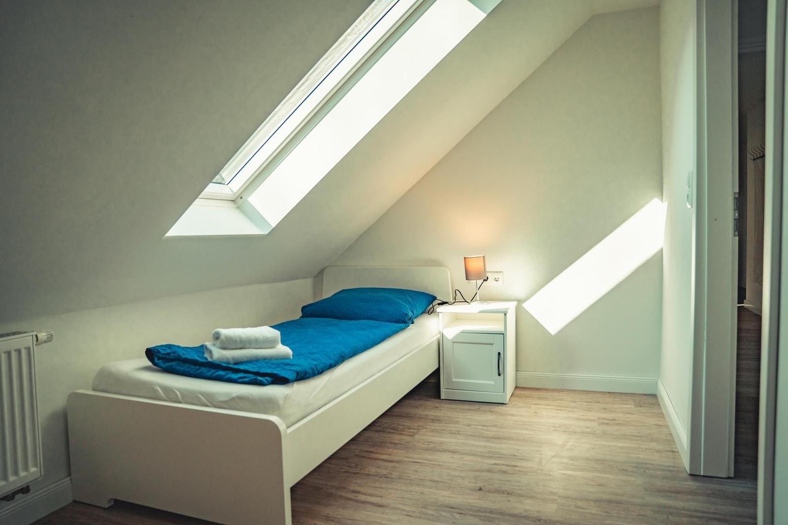 Ein Schlafzimmer mit Dachschräge, Bett, Nachttisch und Dachfenster.