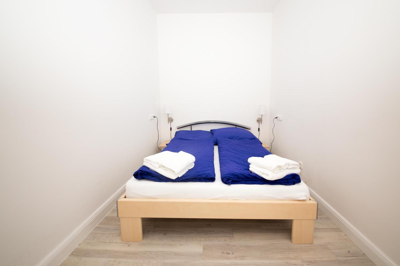 Schlafzimmer mit Bett, blauer Bettwäsche und weißen Handtüchern.