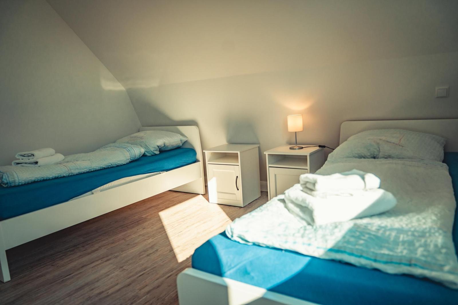 Zwei Betten mit blauen Matratzen und weißen Nachttischen unter schrägem Dach