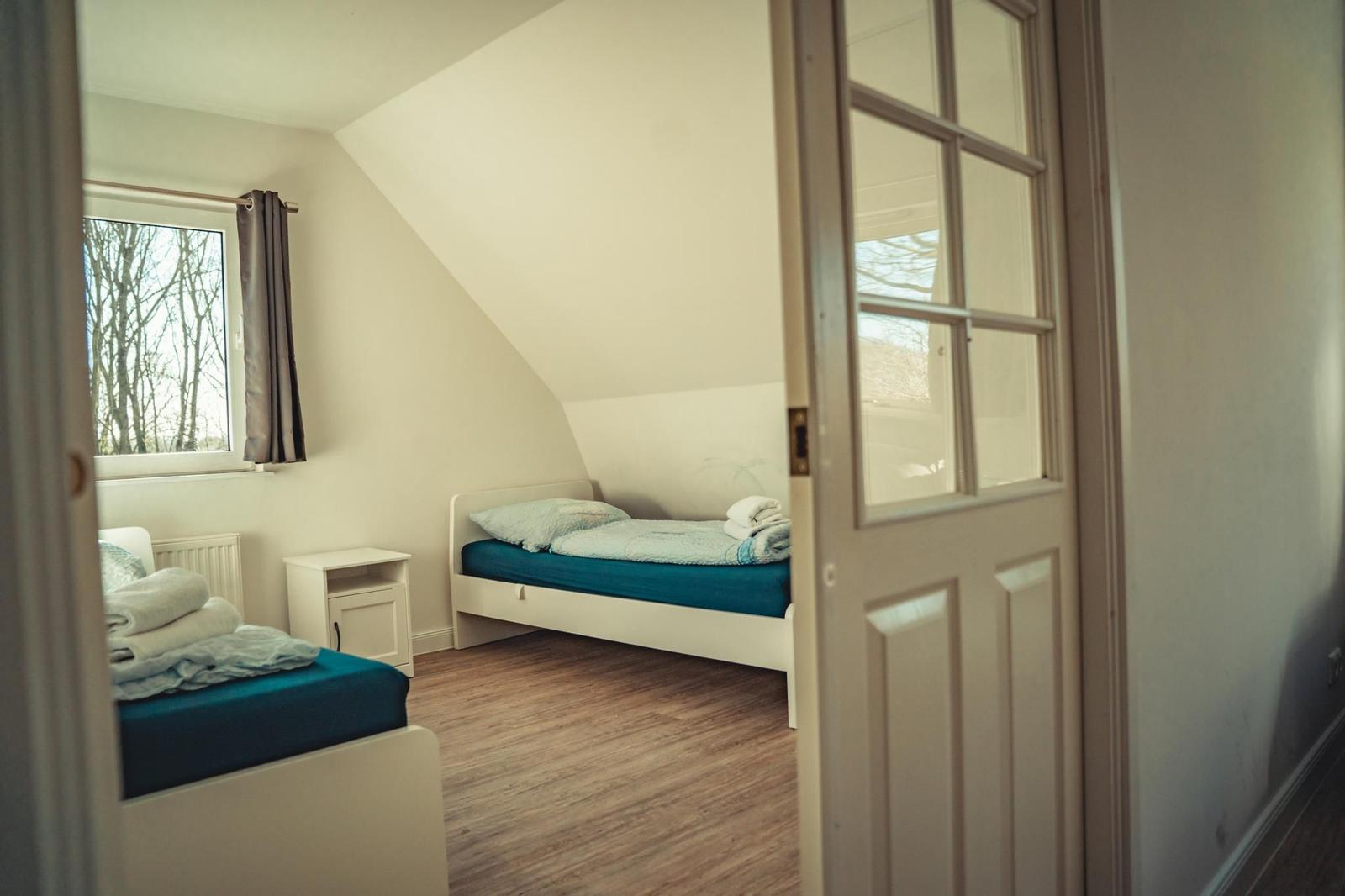 Zimmer mit zwei Betten, Holzboden und Fenster mit Blick auf Bäume.