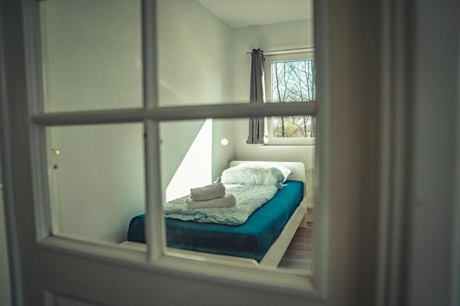 Ein Schlafzimmer mit einem Bett, einem Fenster und einer Tür mit Glasfeldern.