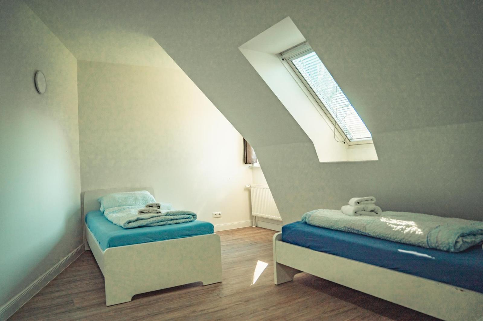 Zwei Einzelbetten in einem Dachzimmer mit Dachfenster und Holzboden.
