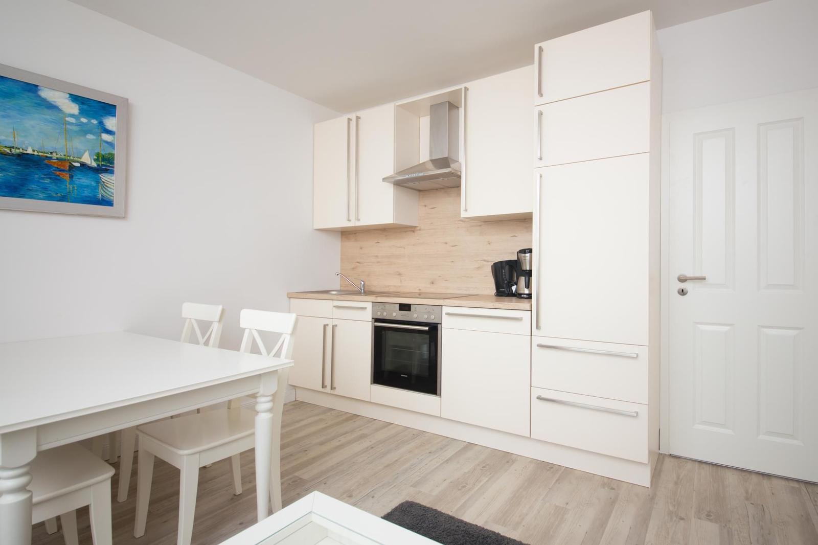 Küche mit Essbereich, weiße Schränke, Holzoptik und Wandbild mit Booten.