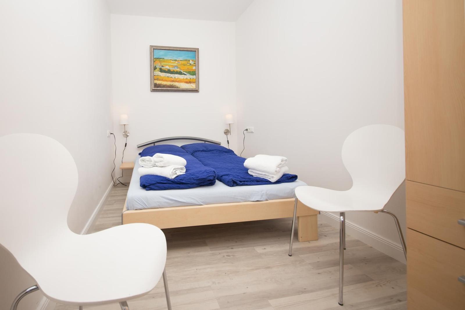 Schlafzimmer mit Bett, zwei Stühlen und Wandbild.