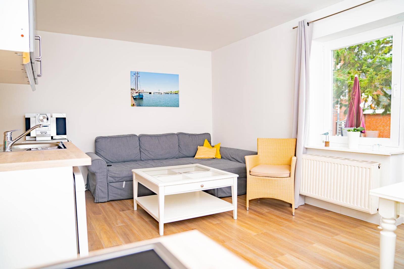 Wohnbereich mit Sofa, Couchtisch und Sessel. Fenster mit Blick nach draußen.