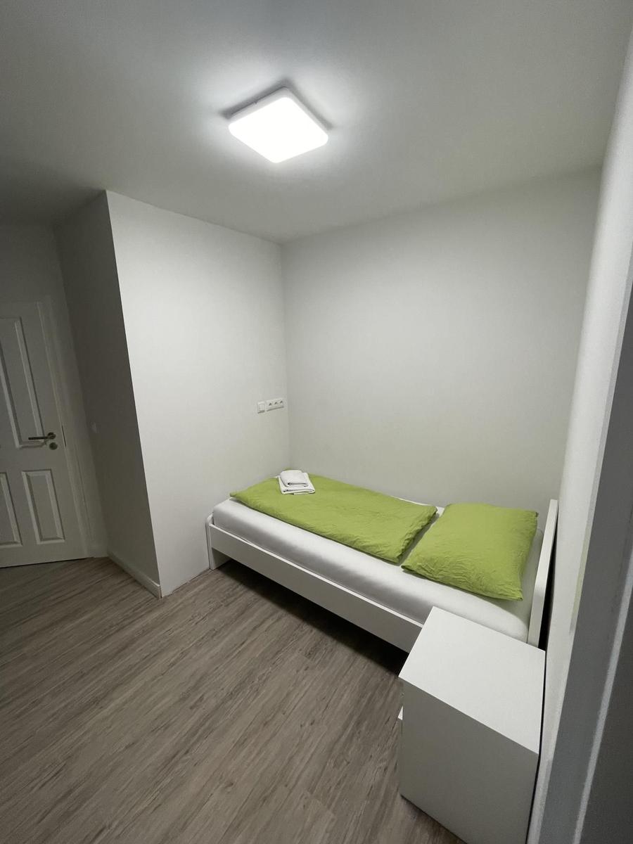 Schlafzimmer mit weißem Bett, grünen Kissen und Holzboden.