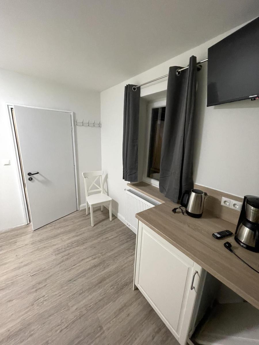 Küche mit Kaffeemaschine und Kessel, Fenster mit Vorhängen und Tür im Hintergrund.