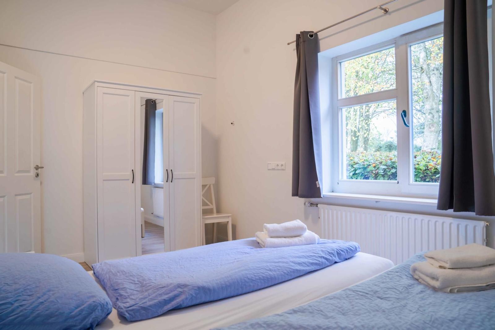 Zimmer mit zwei Betten, Garderobe und Fenster mit Blick auf Grün.