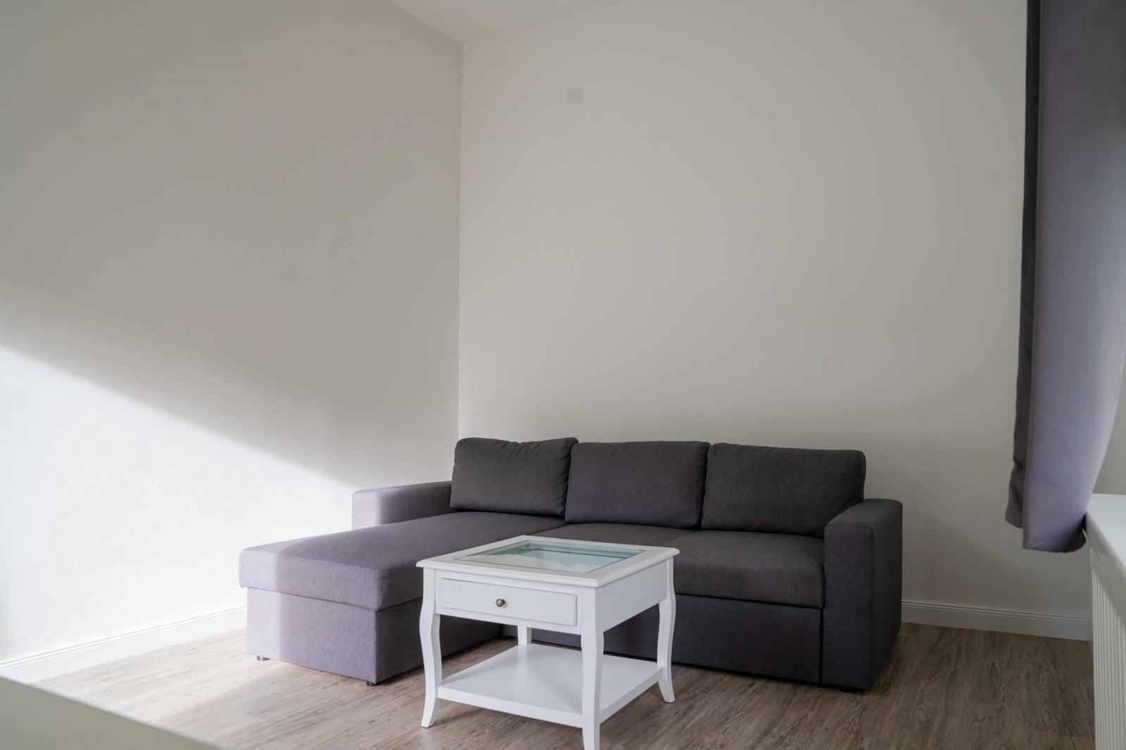 Ein grauer Ecksofa mit weißem Couchtisch auf Holzboden.