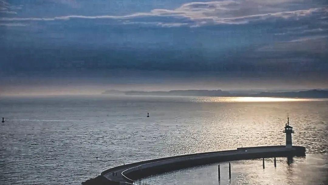 Harbor with lighthouse and view of the sea at sunset.