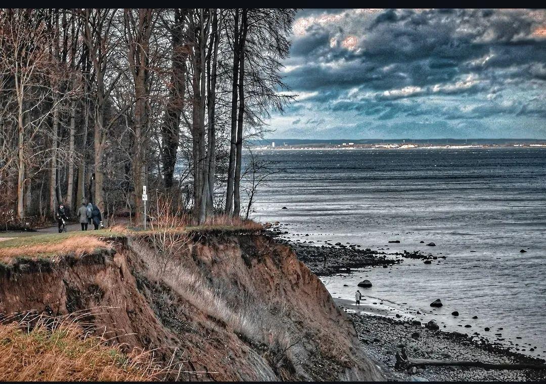 Path along a cliff with view of the sea and trees in the background.