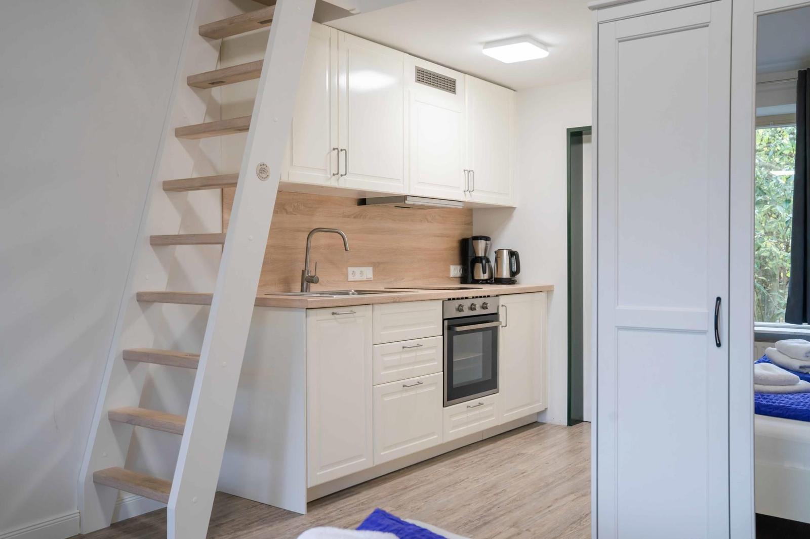 Küche mit weißen Schränken, Herd und Treppe zur oberen Etage.