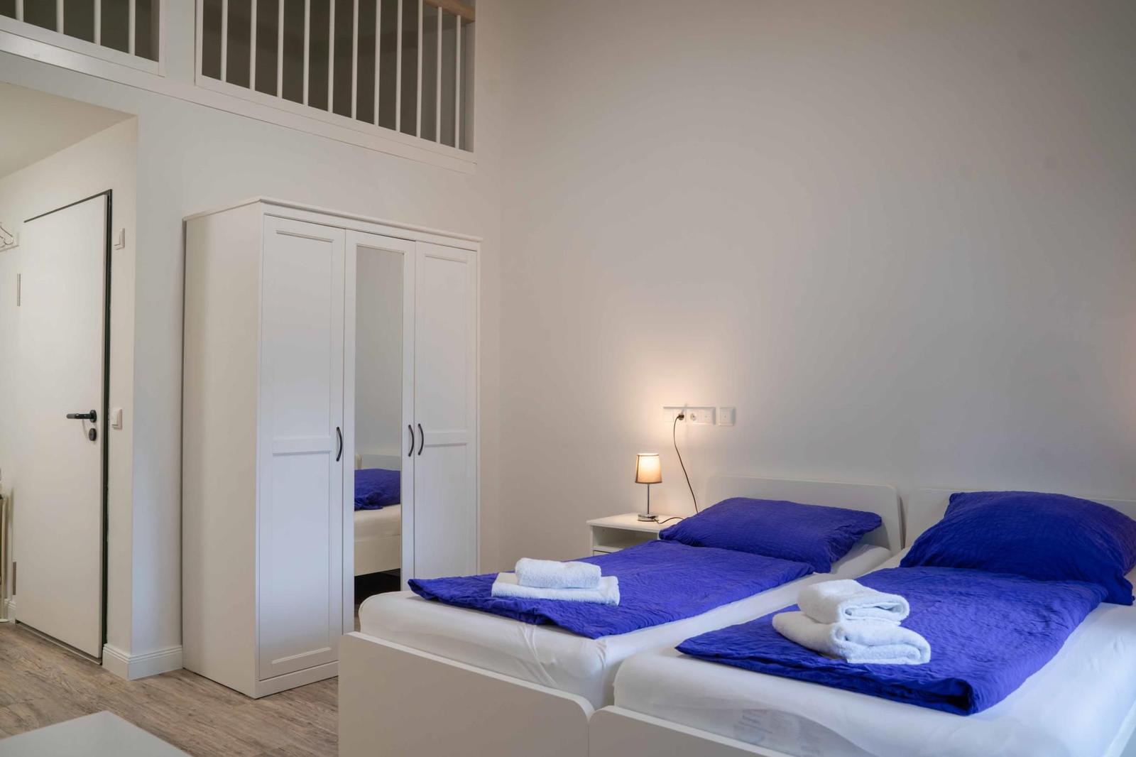 Zwei Betten mit blauen Bettwäsche und weißen Handtüchern. Weißer Kleiderschrank und Nachttisch.